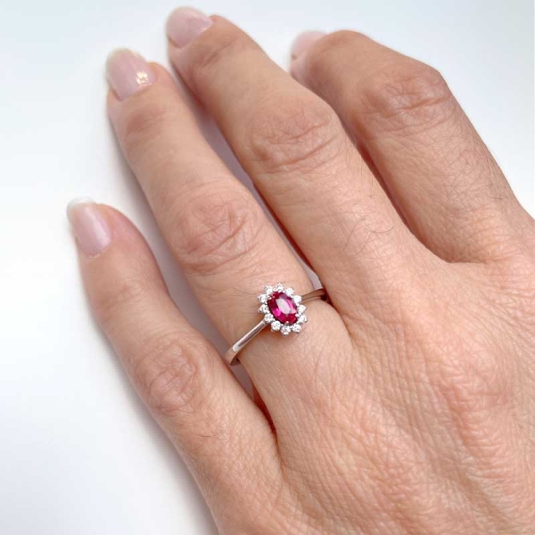 Sortija de estilo clásico con un rubí central en talla oval y orla de diamantes alrededor. Oro blanco de primera ley