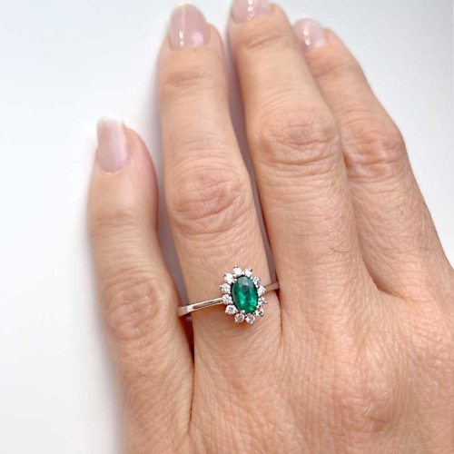 Sortija de estilo clásico con una esmeralda central en talla oval y orla de diamantes alrededor. Oro blanco de primera ley