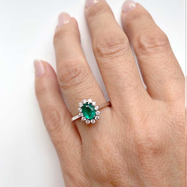 Sortija de estilo clásico con una esmeralda central en talla oval y orla de diamantes alrededor. Oro blanco de primera ley