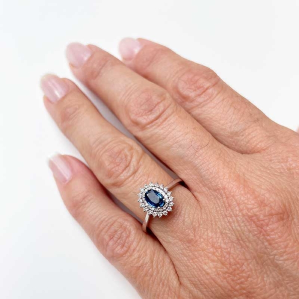 Sortija de estilo clásico con un zafiro central en talla oval y doble orla de diamantes alrededor. Oro blanco de primera ley